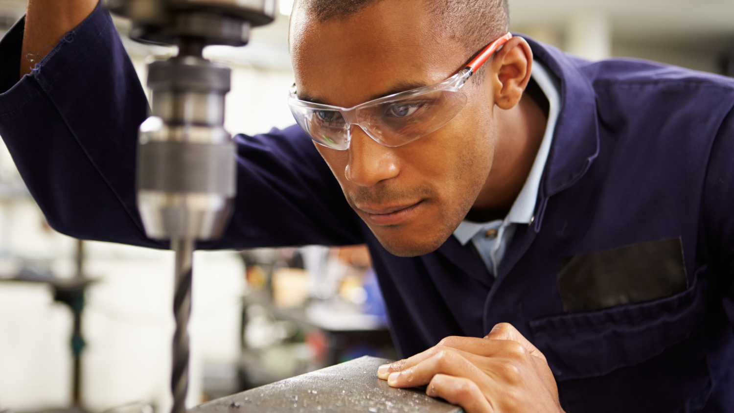 Worker wearing clear prescription safety glasses operating a drill press in workshop