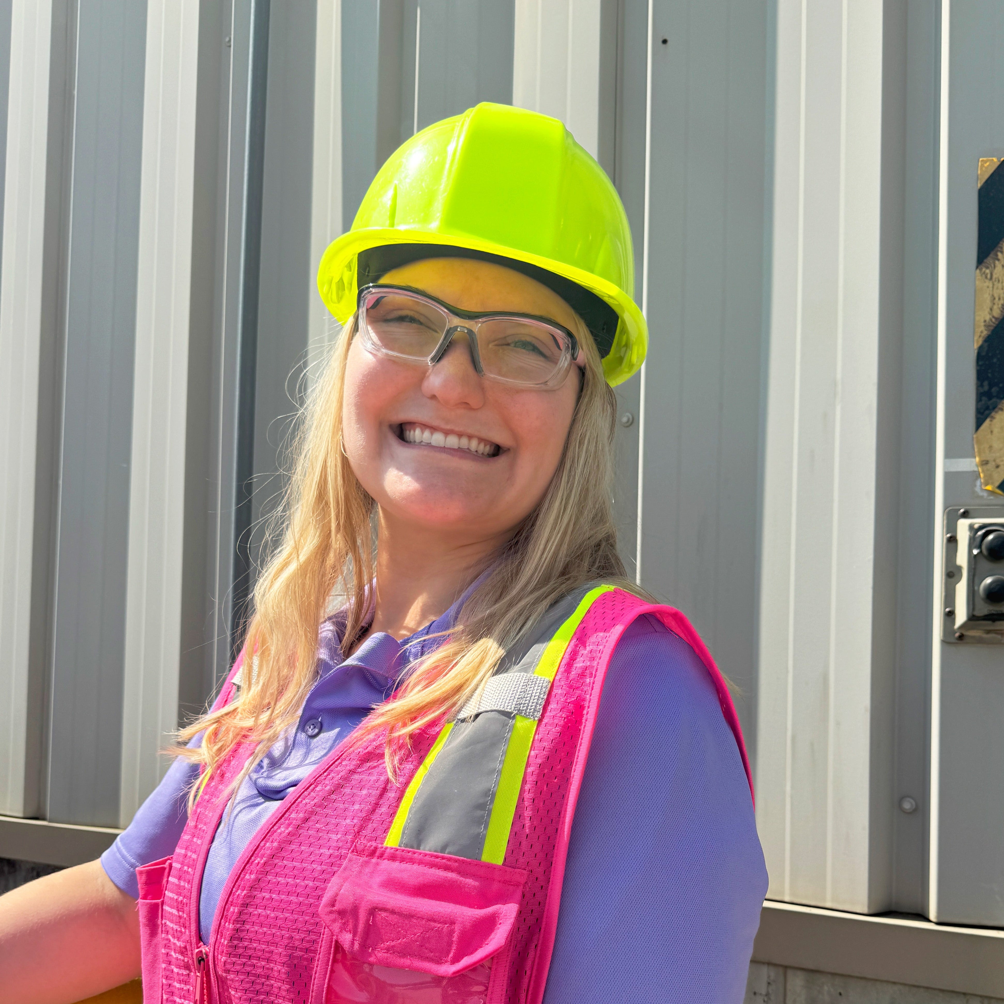 HiDX prescription safety glasses in pink worn by a woman in safety gear at a construction site