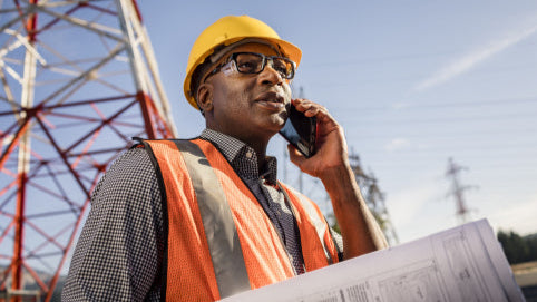 Worker wearing [product name] prescription safety glasses in black, orange vest and yellow hardhat outdoors