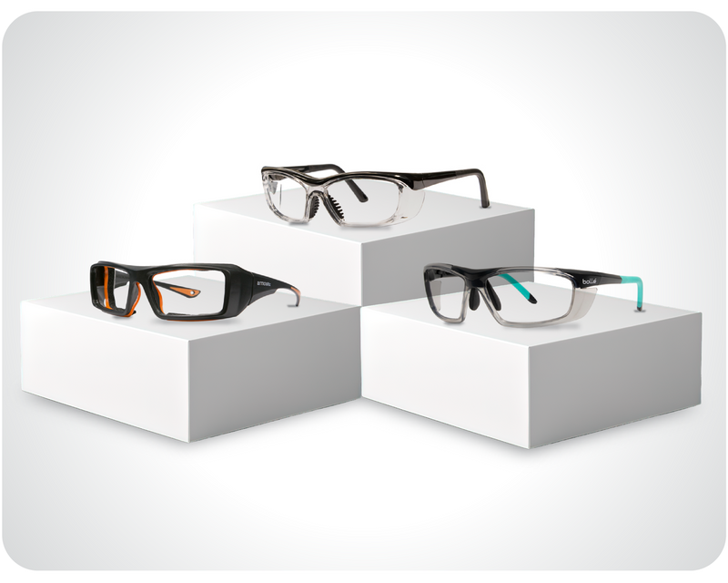 Prescription safety glasses in black, clear, and black-blue variants on white display blocks