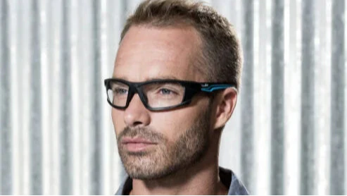 TRON prescription safety glasses in black with blue trim worn by man indoors