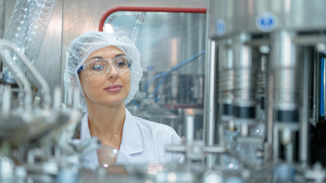 Image of woman wearing food-safe prescription safety glassses and wearing a hair net and white coat in a food processing facility