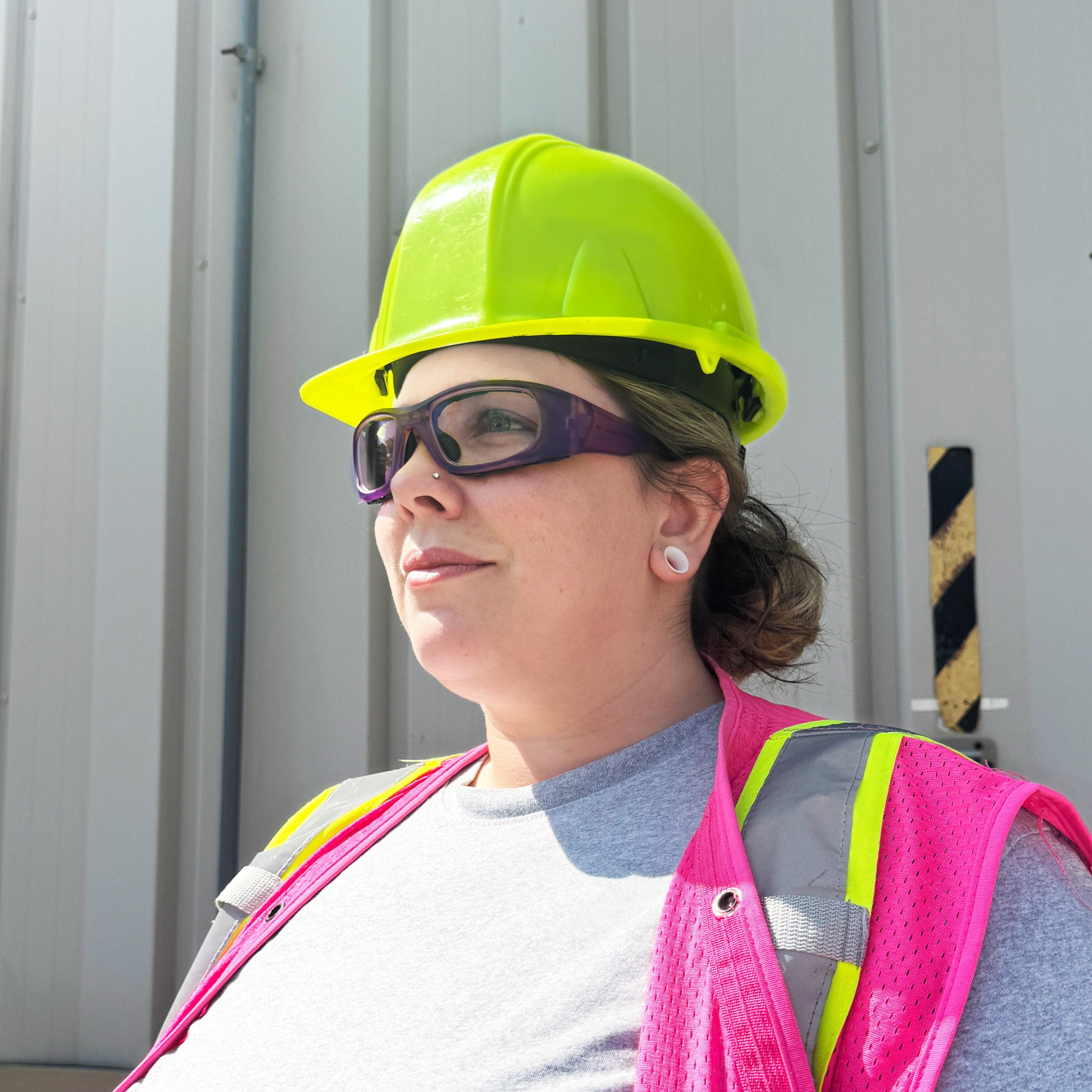 Woman construction worker wearing hard hat and pink safety vest while wearing HiDX A004 prescription safety glasses in purple.