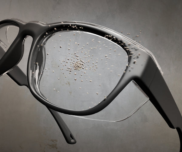 Close-up of a pair of prescription safety glasses with small stones hitting the lenses against a gray background